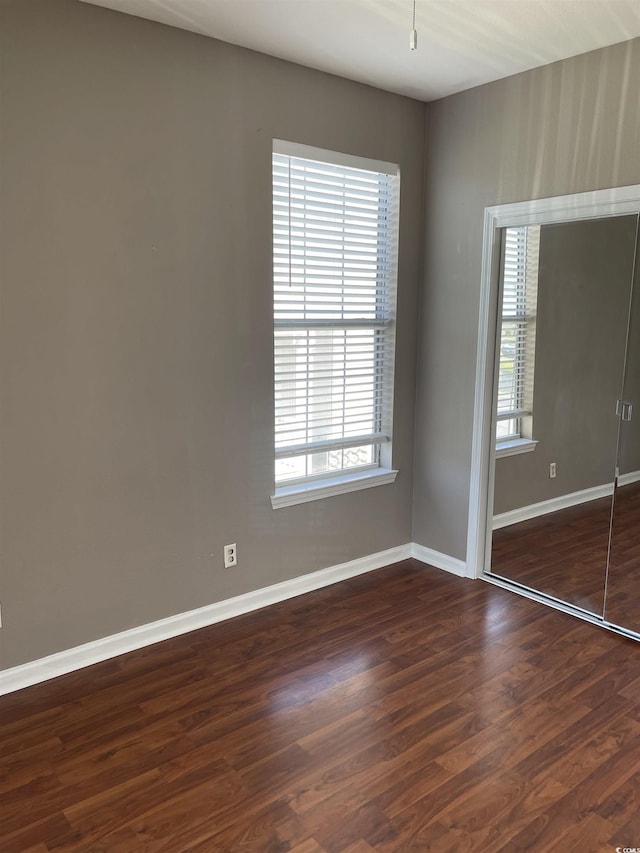 unfurnished bedroom with baseboards, dark wood-style floors, and a closet