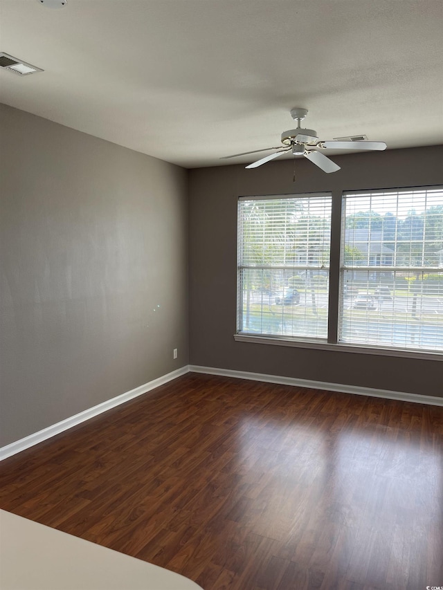 unfurnished room with visible vents, a ceiling fan, baseboards, and dark wood-type flooring