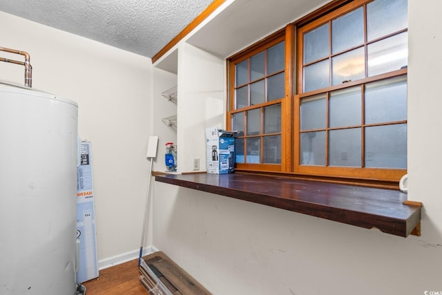 interior details with water heater, a textured ceiling, baseboards, and wood finished floors