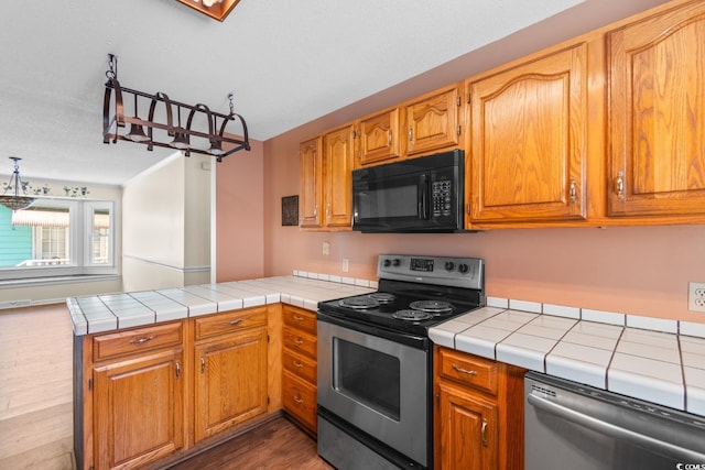 kitchen with dark wood-style floors, a peninsula, appliances with stainless steel finishes, and tile counters