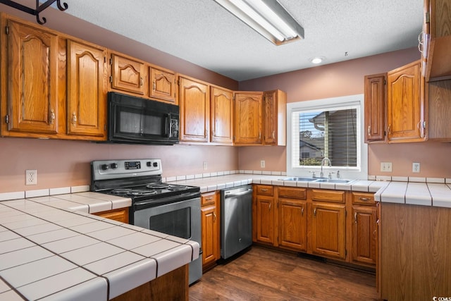 kitchen featuring appliances with stainless steel finishes, a sink, tile counters, and brown cabinets