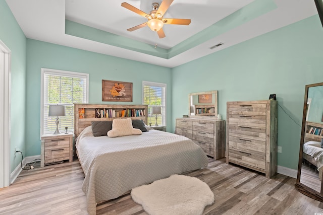bedroom with light wood finished floors, baseboards, a tray ceiling, and a ceiling fan