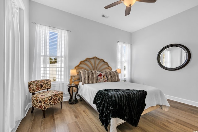 bedroom featuring visible vents, multiple windows, baseboards, and wood finished floors