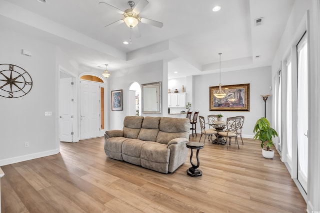 living room featuring visible vents, baseboards, light wood-style floors, and a tray ceiling