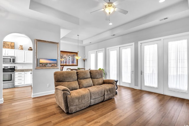 living room with visible vents, light wood-style flooring, baseboards, a raised ceiling, and ceiling fan