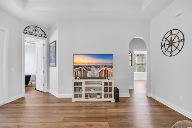 hall with wood finished floors, arched walkways, and baseboards