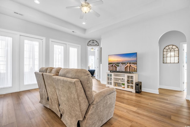 living room with arched walkways, visible vents, light wood-type flooring, and a wealth of natural light