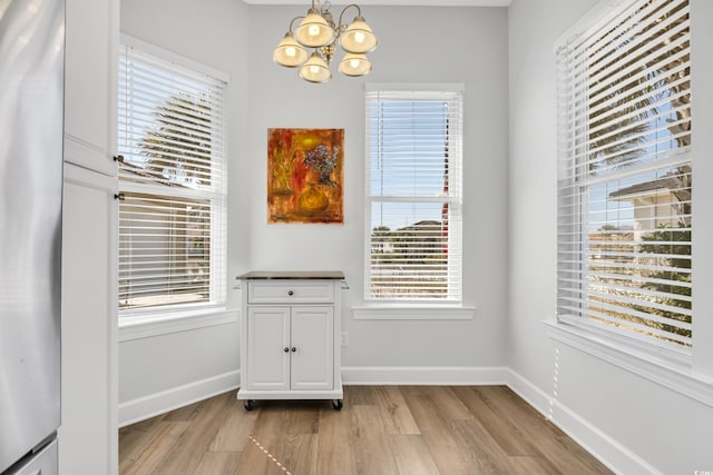 unfurnished dining area with light wood-type flooring, baseboards, a healthy amount of sunlight, and an inviting chandelier