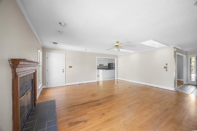 unfurnished living room with a skylight, a tile fireplace, ceiling fan, wood finished floors, and crown molding