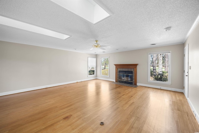 unfurnished living room featuring a healthy amount of sunlight, a skylight, light wood finished floors, and a tile fireplace