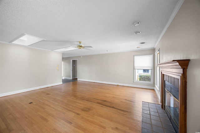 unfurnished living room featuring a skylight, crown molding, a ceiling fan, wood finished floors, and a tile fireplace