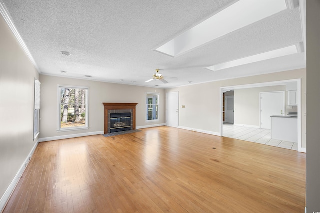 unfurnished living room with a tile fireplace, light wood-style flooring, a skylight, a ceiling fan, and crown molding