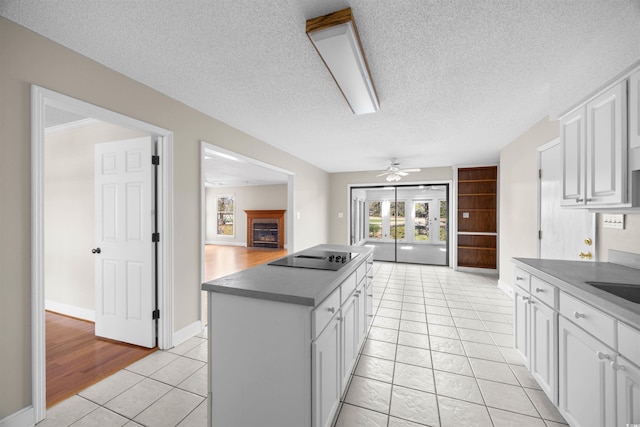 kitchen featuring a fireplace, black electric stovetop, dark countertops, a ceiling fan, and white cabinets