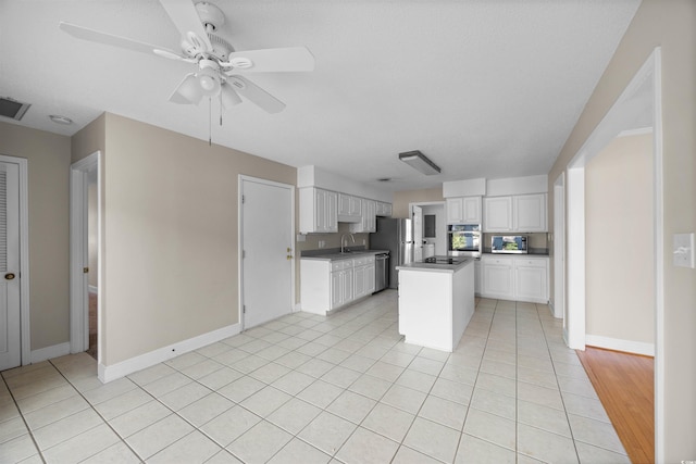 kitchen featuring light tile patterned floors, dark countertops, ceiling fan, appliances with stainless steel finishes, and white cabinetry