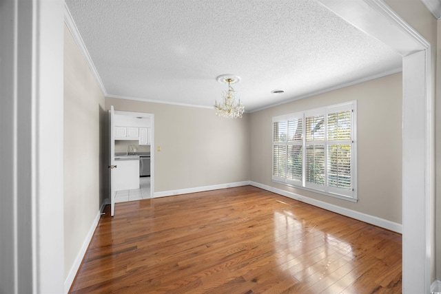 unfurnished room with a chandelier, a textured ceiling, wood finished floors, baseboards, and crown molding