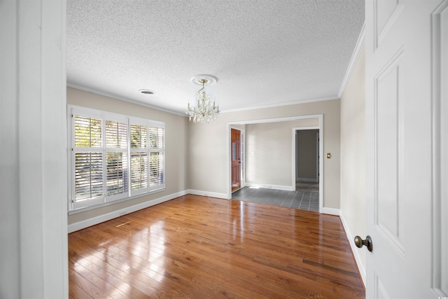 empty room featuring a textured ceiling, a notable chandelier, crown molding, and wood finished floors