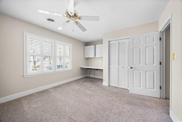 unfurnished bedroom with light colored carpet, a closet, built in study area, and visible vents