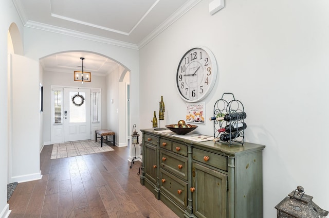 foyer featuring ornamental molding, arched walkways, dark wood-style flooring, and baseboards