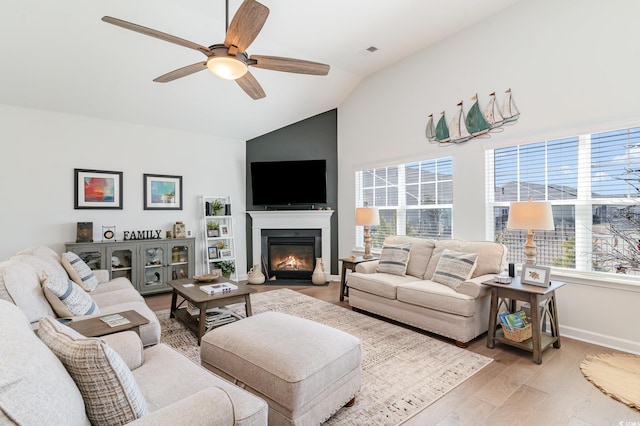 living area with light wood-style flooring, a fireplace with flush hearth, vaulted ceiling, ceiling fan, and baseboards