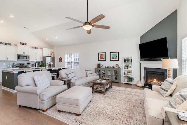 living area with recessed lighting, a fireplace with flush hearth, a ceiling fan, wood finished floors, and high vaulted ceiling