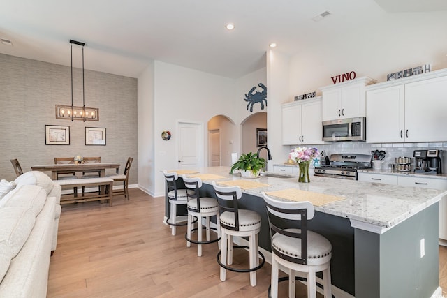 kitchen featuring arched walkways, a towering ceiling, appliances with stainless steel finishes, light wood-type flooring, and a sink