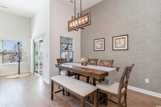 dining space with wallpapered walls, an accent wall, baseboards, and wood finished floors