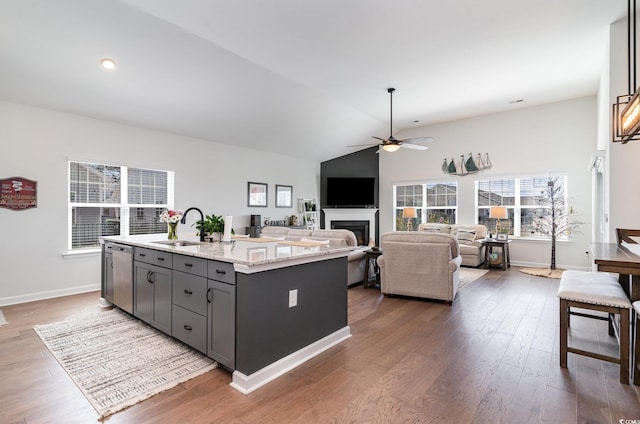 kitchen featuring a fireplace, a sink, vaulted ceiling, dishwasher, and an island with sink