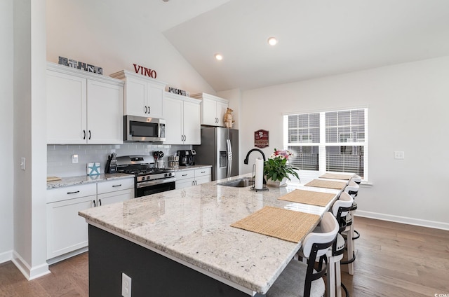 kitchen with lofted ceiling, a sink, appliances with stainless steel finishes, tasteful backsplash, and an island with sink