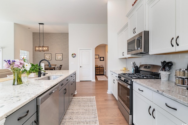 kitchen with arched walkways, a sink, light wood-style floors, appliances with stainless steel finishes, and backsplash