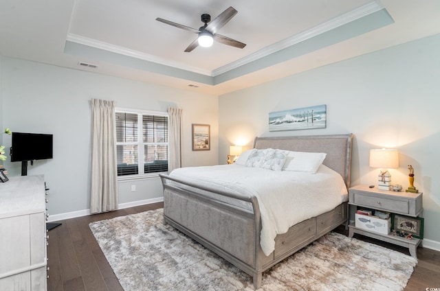 bedroom with a tray ceiling, wood finished floors, visible vents, and baseboards