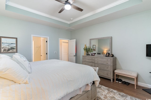 bedroom featuring ornamental molding, a raised ceiling, baseboards, and wood finished floors