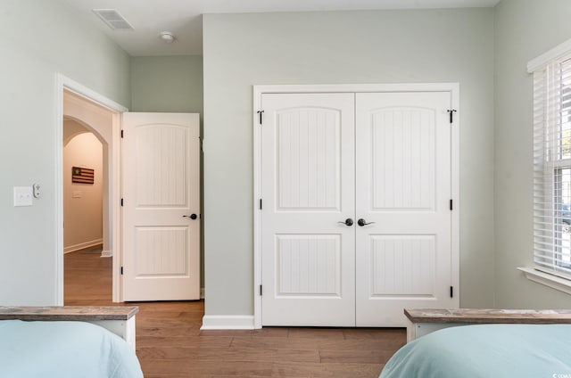 bedroom featuring baseboards, visible vents, arched walkways, wood finished floors, and a closet