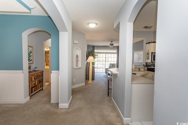 hall featuring a textured ceiling, arched walkways, light carpet, a wainscoted wall, and visible vents