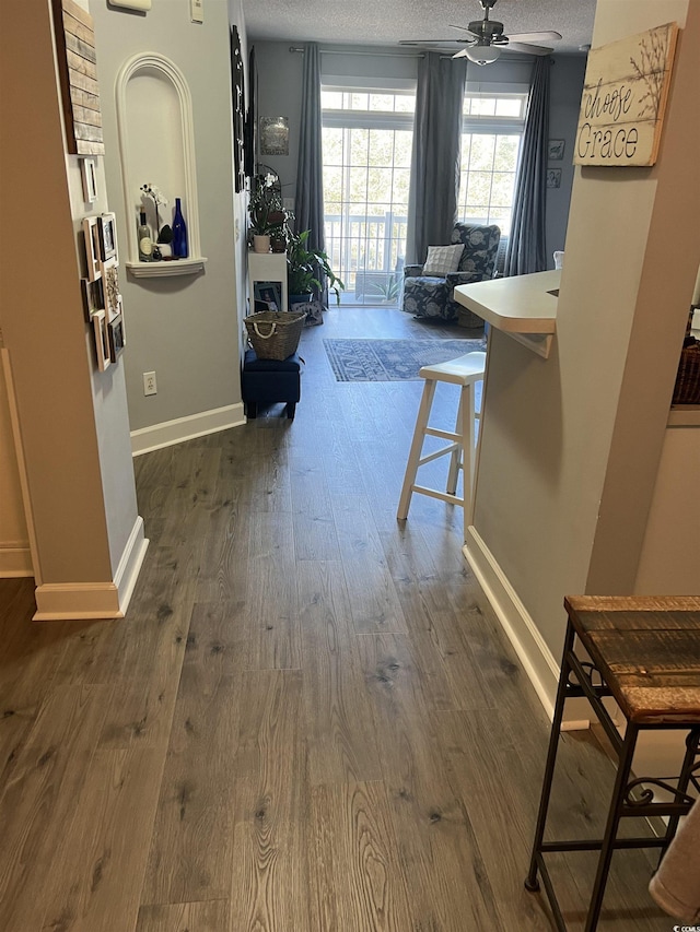 hallway with a textured ceiling, baseboards, and dark wood-style flooring