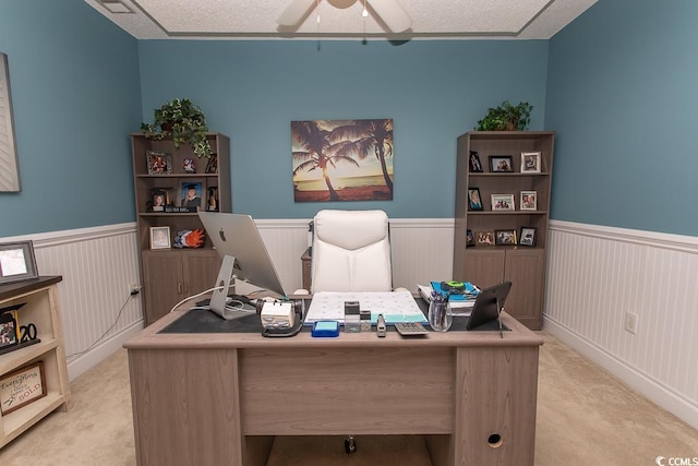 office featuring light carpet, a textured ceiling, wainscoting, and a ceiling fan