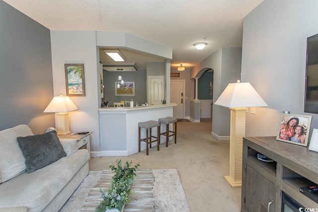 living room featuring baseboards, arched walkways, a textured ceiling, and light colored carpet