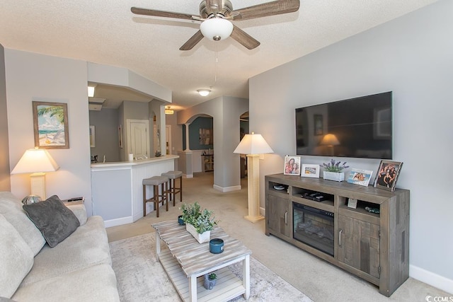 living room featuring arched walkways, a textured ceiling, light carpet, and a ceiling fan