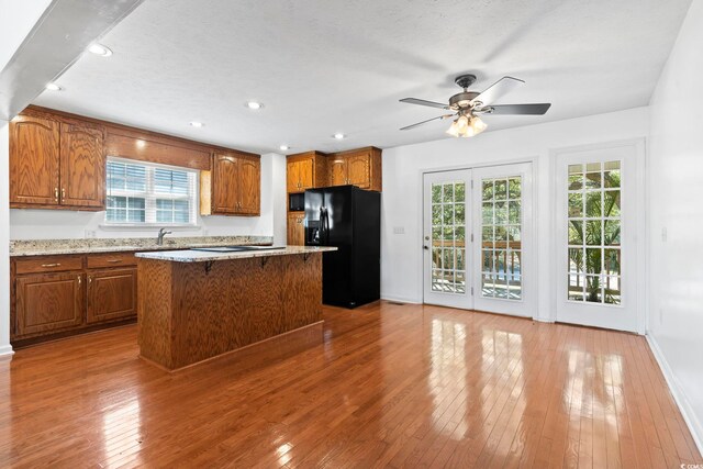 kitchen featuring a kitchen island, black fridge with ice dispenser, light wood-style floors, brown cabinets, and plenty of natural light