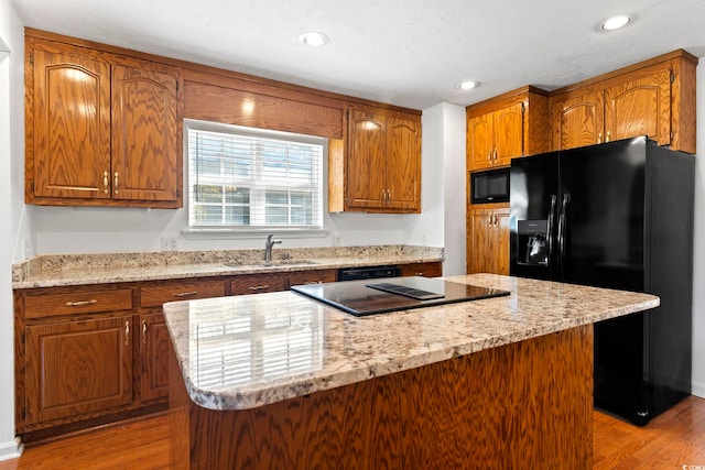 kitchen featuring light wood-style flooring, brown cabinetry, a kitchen island, a sink, and black appliances