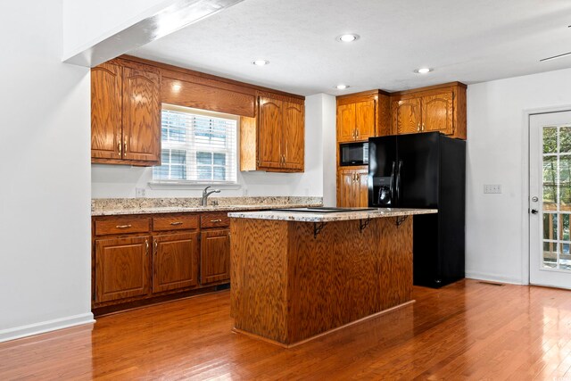 3615 Sunfish St, Murrells Inlet, SC 29576 - kitchen with a kitchen breakfast bar, wood finished floors, brown cabinetry, a kitchen island, and black appliances