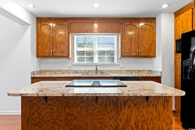 kitchen with black appliances, light stone counters, brown cabinets, and a sink