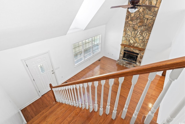 stairway with baseboards, a ceiling fan, wood finished floors, a stone fireplace, and high vaulted ceiling