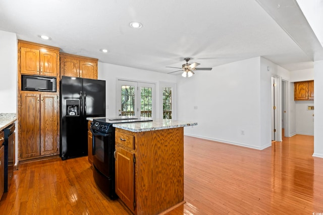 kitchen with brown cabinets, recessed lighting, a kitchen island, wood finished floors, and black appliances