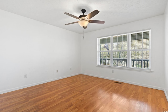 empty room with wood finished floors, visible vents, and baseboards