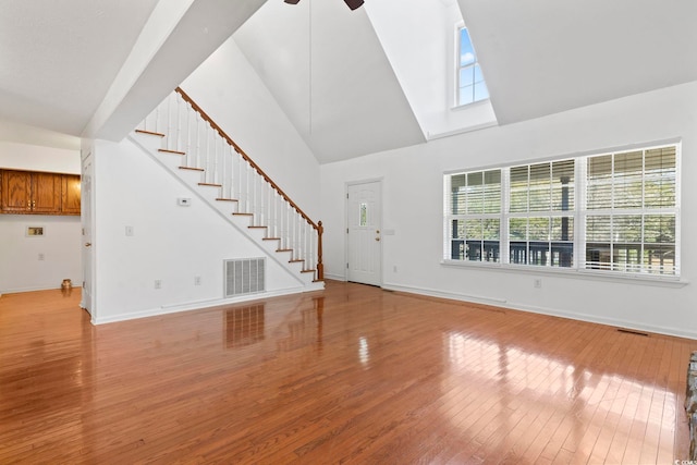 unfurnished living room with light wood finished floors, baseboards, visible vents, stairs, and high vaulted ceiling