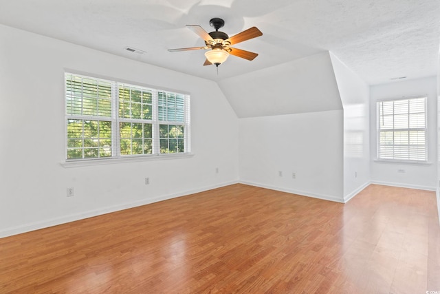 additional living space featuring plenty of natural light, light wood-type flooring, lofted ceiling, and visible vents