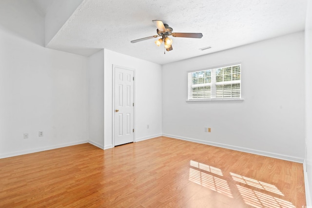 spare room featuring light wood-style floors, ceiling fan, baseboards, and a textured ceiling