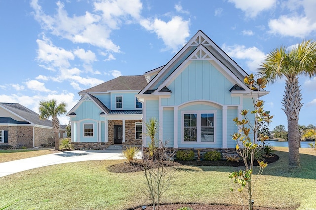 view of front of house with concrete driveway, board and batten siding, a front yard, a standing seam roof, and stone siding