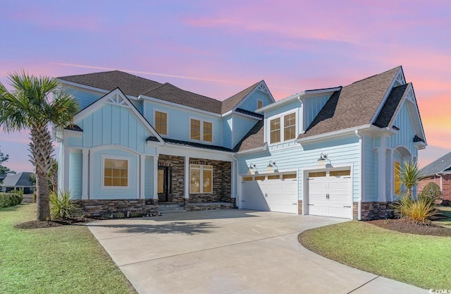 view of front facade featuring a shingled roof, concrete driveway, stone siding, board and batten siding, and a front yard