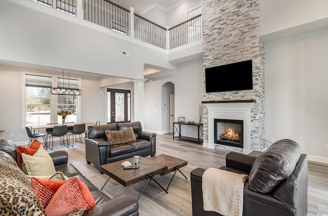 living area featuring light wood finished floors, visible vents, baseboards, crown molding, and a stone fireplace